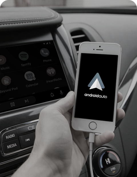 Hand holding smartphone with Android Auto connected to car dashboard display for navigation, music, and hands-free control