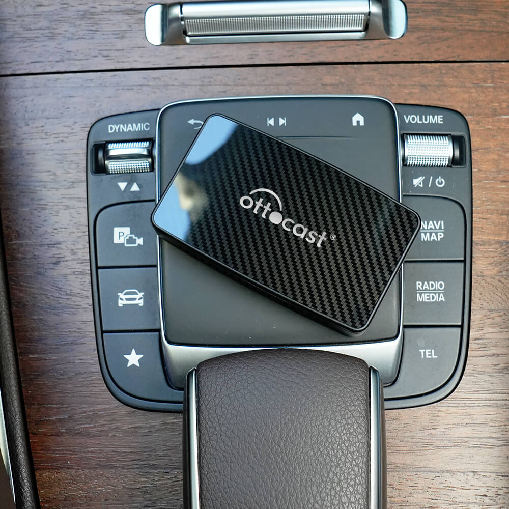 Ottocast Play2Video Pro wireless CarPlay and Android Auto adapter on car control panel with carbon fiber design.
